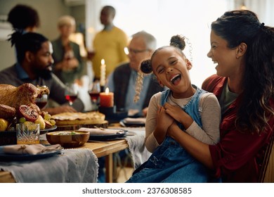Happy African American girl and her mother laughing while gathering with their extended family on Thanksgiving at home.