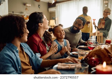 Happy African American girl laughing while enjoying in Thanksgiving dinner with her extended family in dining room.