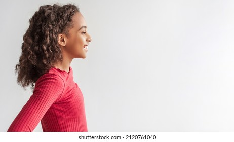 Happy African American Girl Looking Aside At Free Space For Text Smiling To Camera Standing Posing On Gray Studio Background, Wearing Casual Clothes. Panorama, Side View Shot