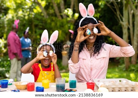 Happy african american girl and mother playing with easter eggs while family in background. unaltered, lifestyle, easter day, art, celebration, family, cultures and holiday concept.