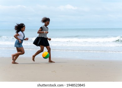 Happy African American girls playing beach football together along the tropical beach on vacation in the summertime. Group of a family having fun at the seashore in the summer travel holiday.