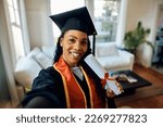 Happy African American graduate student taking selfie after receiving university certificate.