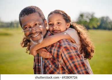 happy african american granddaughter hugging her smiling grandfather on green lawn 