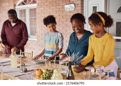 Happy African American Grandmother With Grandkids Preparing Table For Family Meal On A Patio. 