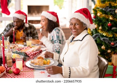 Happy african american grandmother wearing santa hat sitting at christmas table with family. family christmas time and festivity together at home. - Powered by Shutterstock