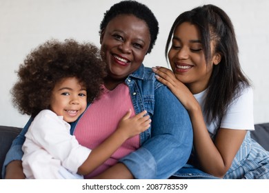 happy African American granny smiling at the camera while daughter and granddaughter hugging her at home