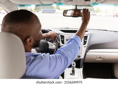Happy African American Guy Adjusting Rear View Mirror, Enjoying New Auto, Sitting On Driver's Seat In Luxury Vehicle. Man Testing Visibility, Over Shoulder View From The Back Passenger Seat
