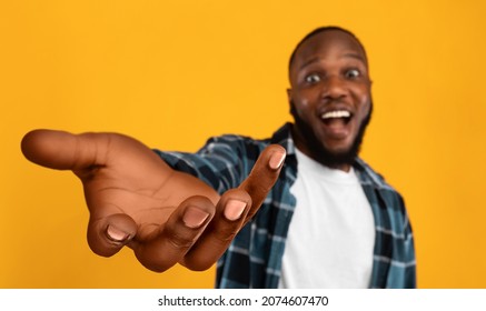 Happy african american guy outstretching hand, holding something invisible on his huge palm, giving it away or asking for something, orange studio background, collage, panorama with copy space - Shutterstock ID 2074607470