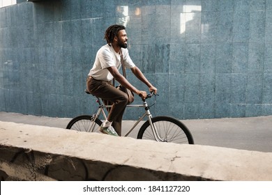 Happy african american guy smiling while riding bicycle at city street - Powered by Shutterstock