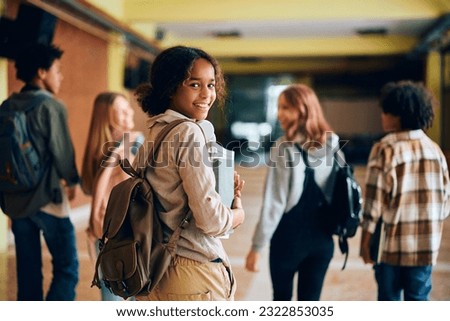 Happy African American high school student walking through hallway with her friends and looking at camera.