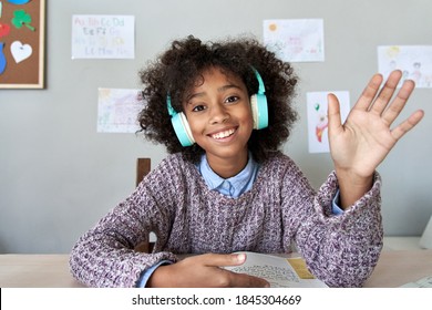 Happy african american kid child girl wearing headphones waving hand talking with remote teacher on social distance learning video conference call zoom class, headshot zoom portrait, web cam view.