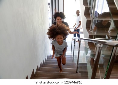 Happy African American Kid Girl Running Up Stairs Into New Big House With Black Parents, Excited Child Daughter Having Fun Exploring Own Home, Afro Family Moving Day Concept, Relocation, Mortgage