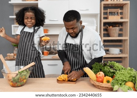 Happy African American kid girl cooking salad with father in kitchen at home	