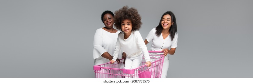 happy african american kid in shopping cart near mother and granny isolated on grey, banner