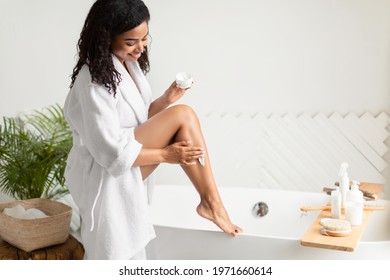 Happy African American Lady Applying Moisturizer Cream On Legs Caring For Body And Moisturizing Skin After Shaving Sitting On Bathtub In Bathroom At Home. Aftershave Skincare Routine Concept - Powered by Shutterstock