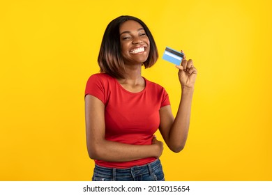 Happy African American Lady Holding Credit Card Advertising Bank Service Posing In Studio On Yellow Background, Smiling To Camera. Easy Banking, Money And Payment Concept