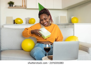 Happy African American Lady Looking At Laptop Receiving Gift From Friends, Celebrating B-day Via Video Call At Home. Virtual Holiday Celebration And Presents Delivery Concept