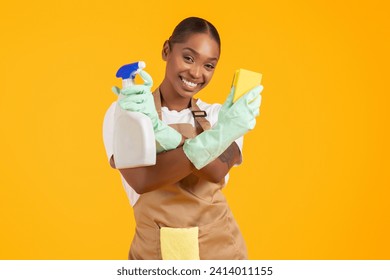 Happy african american lady showing cleaning supplies holding detergent spray and sponge over yellow studio background, wearing apron. Spring cleanup service offer concept - Powered by Shutterstock