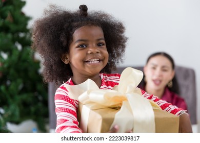 Happy African American little girl holding Christmas gift box or presents gift at home. Merry Christmas and Happy Holidays. Happy family on Christmas - Powered by Shutterstock