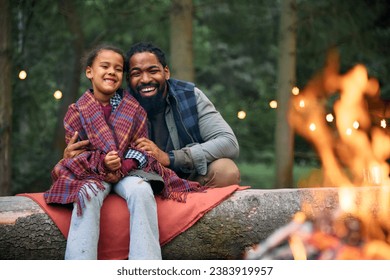 Happy African American little girl and her father relaxing by campfire at trailer park. - Powered by Shutterstock