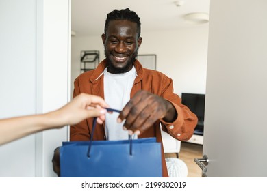 Happy African American Male Customer Receiving Colorful Shopping Bag, Woman Delivering His Order, Guy Standing At Door Of His Home And Smiling