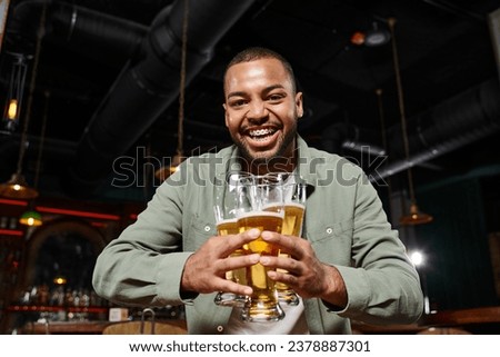 happy african american man with braces holding three glasses of beer in bar, having fun on weekends