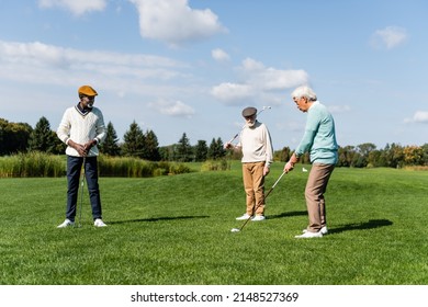 happy african american man in flat cap looking at asian friend playing golf - Powered by Shutterstock