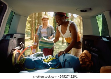 Happy African American man and his girlfriend packing their luggage while going on camping with their van. - Powered by Shutterstock