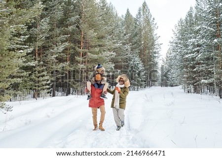 Happy African American man, his wife and son having stroll in fresh air on frosty winter day among coniferous trees covered with snow