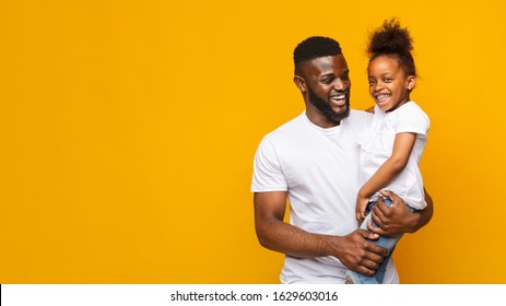 Happy african american man holding little smiling daughter over yellow studio background, panorama with copy space
