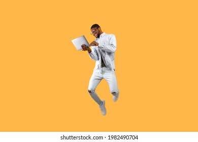 Happy African American Man Jumping Up With Laptop Computer, Having Fun On Yellow Studio Background. Young Black Guy Gambling Online Successfully, Using Pc. Full Length