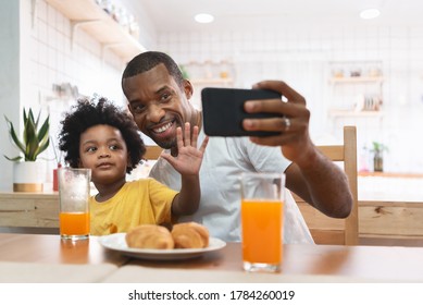 Happy African American man and kid boy using mobile phone for taking selfie together at home. African Father and son doing video chat and waving hand while talking to family with smartphone. BeH3althy - Powered by Shutterstock