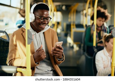 Happy African American Man Listening Music Over Headphones And Using Mobile Phone While Commuting By Bus. 