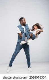 happy african american man playing with thrilled daughter while holding her in hands on grey - Shutterstock ID 2028076334