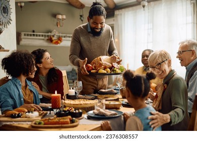 Happy African American man serving traditional roast turkey while gathering with his family for Thanksgiving at dining table. - Powered by Shutterstock