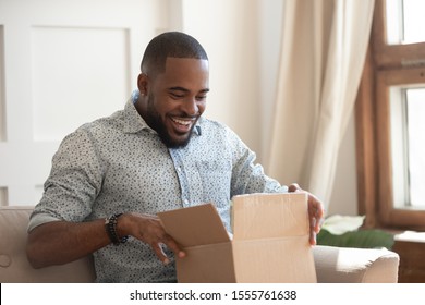 Happy african american man sit on couch feel excited opening cardboard box delivery parcel, smiling biracial millennial male shopping online unpack unbox online order, overjoyed with service or goods - Powered by Shutterstock