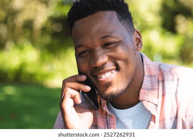 Happy african american man sitting on stairs and talking on smartphone in sunny garden, copy space. Outdoors, expression, gesticulation, technology, communication and nature, unaltered. - Powered by Shutterstock