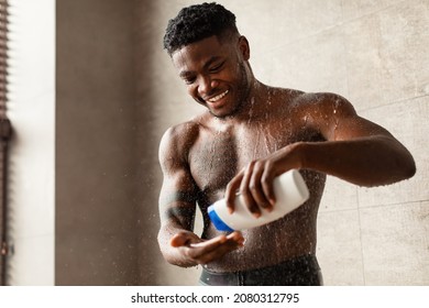 Happy African American Man Squeezing Shower Gel Bottle Washing Body Standing Under Falling Water In Modern Bathroom Indoors. Male Bodycare Routine And Beauty Products. Selective Focus