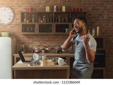 Happy african american man talking on smartphone while baking in kitchen