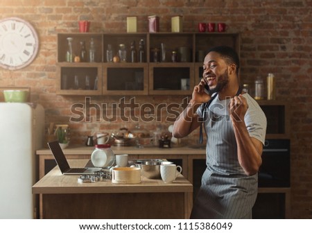 Happy african american man talking on smartphone while baking in kitchen