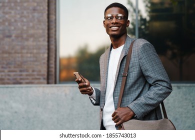 Happy african american man using mobile phone while walking on street - Powered by Shutterstock