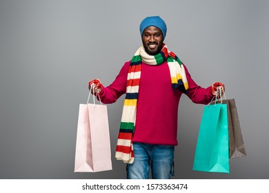 Happy African American Man In Winter Outfit With Shopping Bags On Grey Background