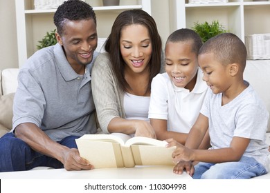 A Happy African American Man, Woman And Boys, Father, Mother And Two Sons, Family Sitting Together At Home Reading A Book