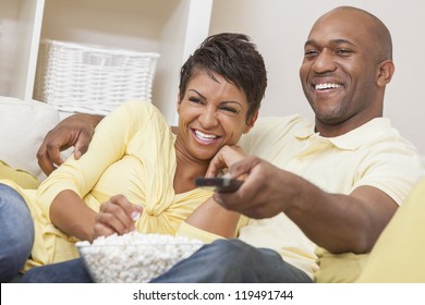 A Happy African American Man And Woman Couple In Their Thirties Sitting At Home, Eating Popcorn And Using Remote Control Watching A Movie Or Television