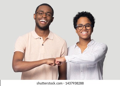 Happy african American man and woman friends isolated on grey studio background give fists bump look at camera, smiling biracial black diverse people in glasses make deal show unity and cooperation - Shutterstock ID 1437938288