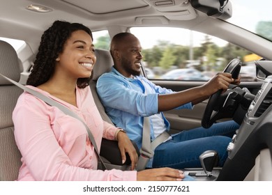 Happy African American man and woman going on summer vacation by car. Beautiful millennial couple sitting inside their new auto, young family cheerfully smiling looking at road, profile side view
