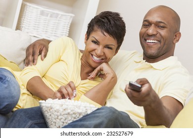 A Happy African American Man And Woman Couple In Their Thirties Sitting At Home Using A Remote Control, Eating Popcorn And Watching A Movie Or Television