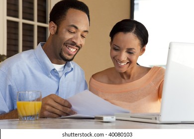 A Happy African American Man And Woman Couple In Their Thirties Working On A Laptop Computer And Looking At Paperwork