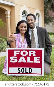 A Happy African American Man And Woman Couple Outside A Large House With A For Sale Sold Sign Celebrating The Purchase Of A Property