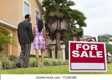 A Happy African American Man And Woman Couple House Hunting Outside A Large House With A For Sale Sign. The Focus Is On The Sign.